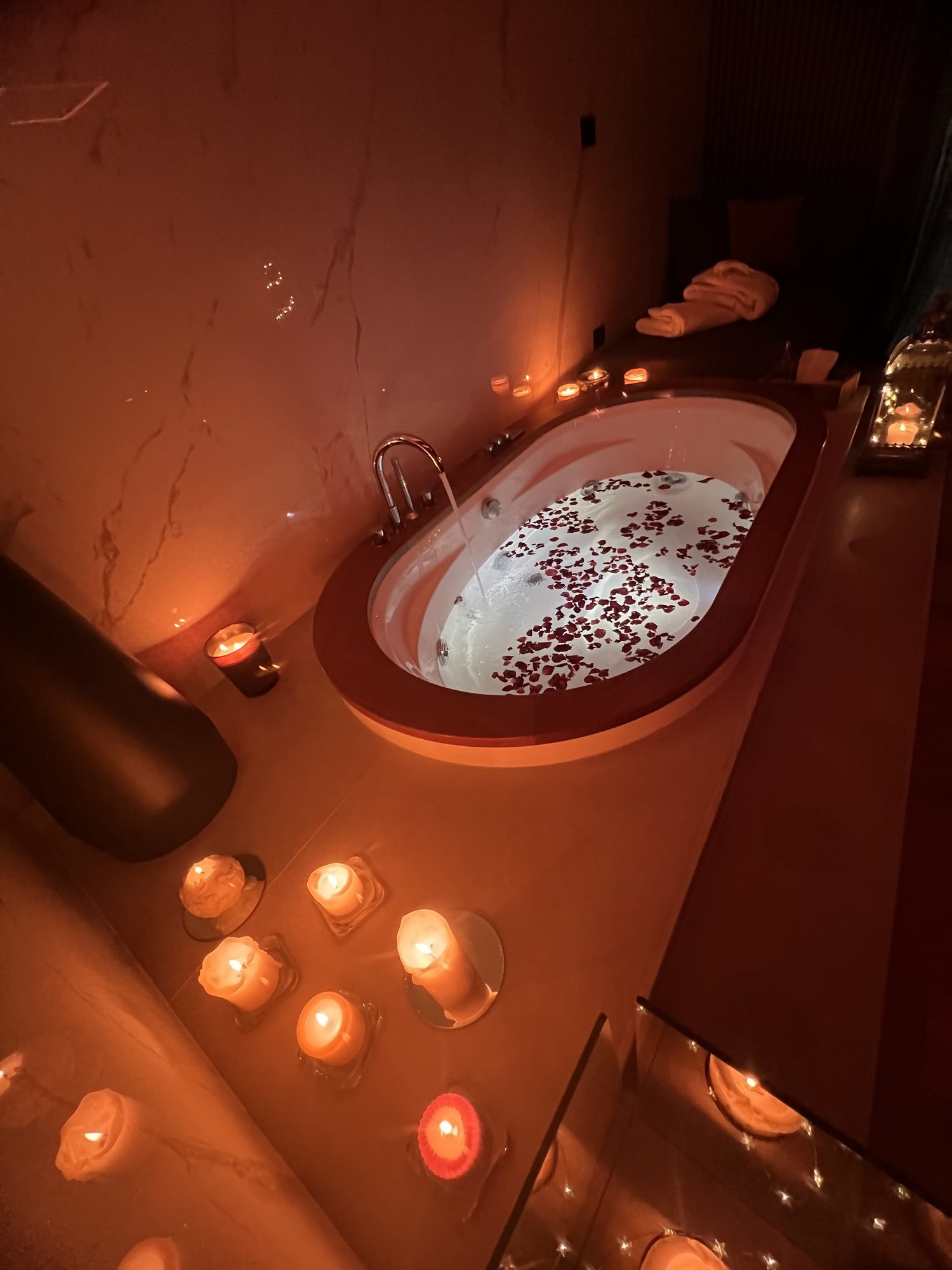 Vasca idromassaggio cosparsa di petali di rosa e circondata di candele, spa privata