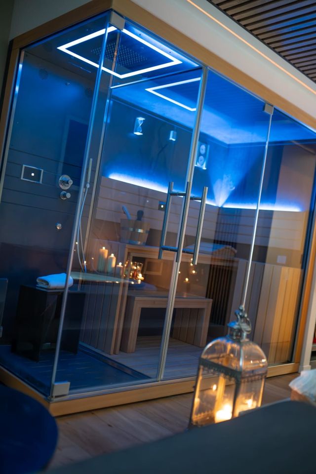 Bagno turco con doccia emozionale a luce blu e sauna in legno oltre il vetro
